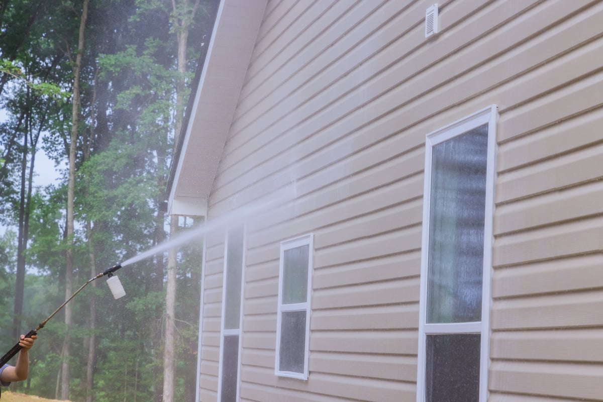 Cleaning a home's exterior siding with a low-pressure spray to remove dirt and stains